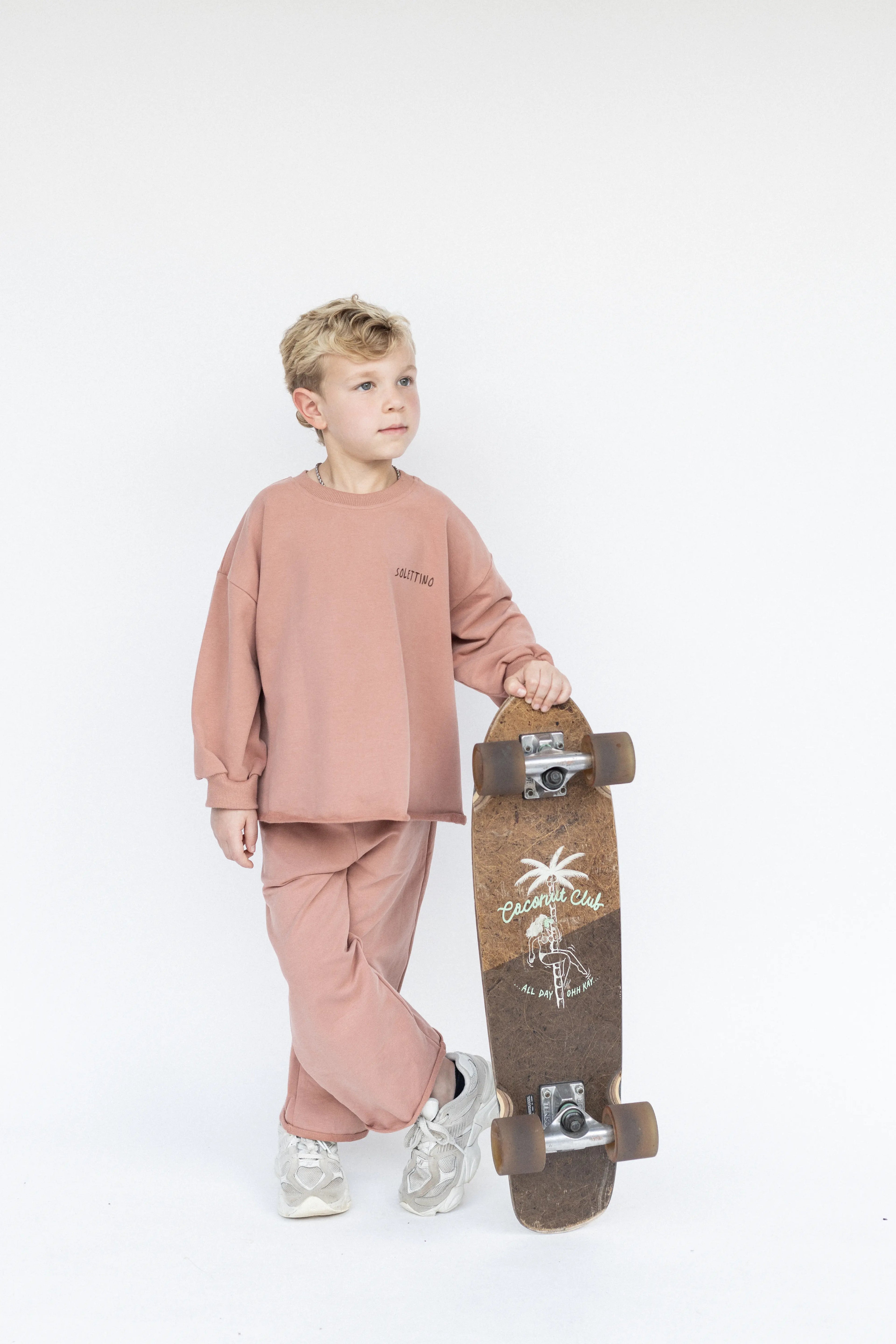 Child in pink outfit holding a skateboard on a white background