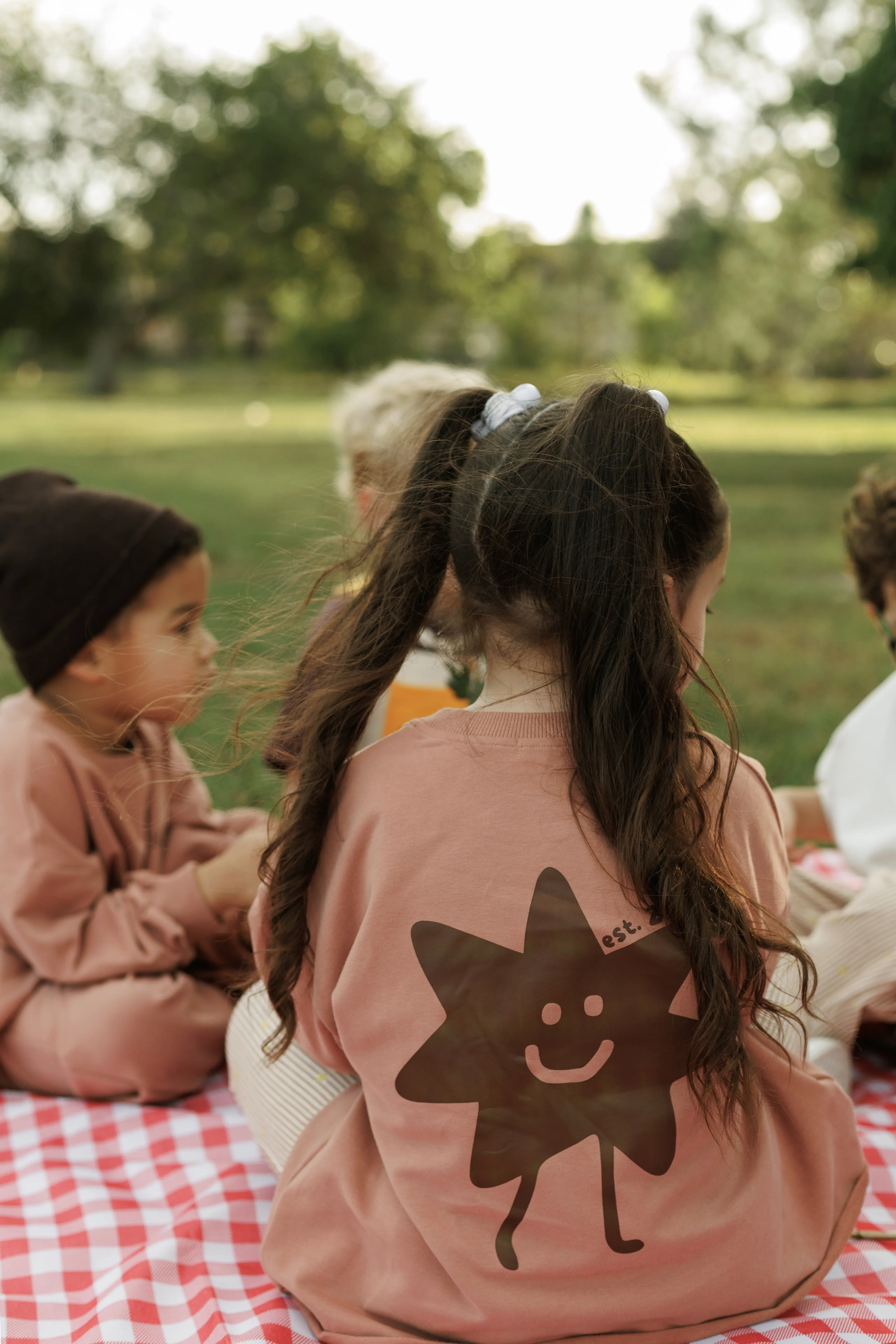 Children sitting on a blanket in a park with one child wearing behind the star set