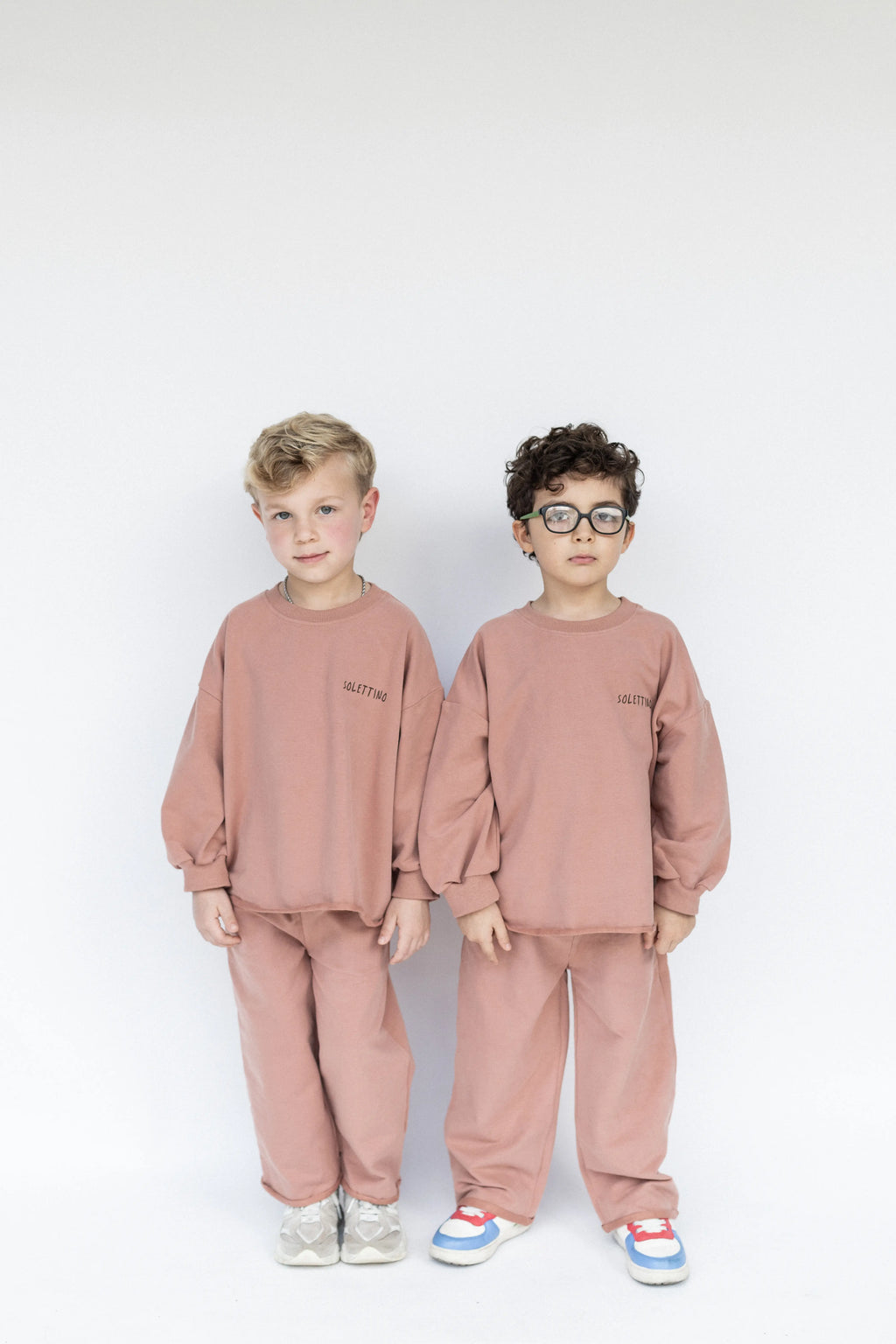 Two children wearing matching pink outfits on a white background