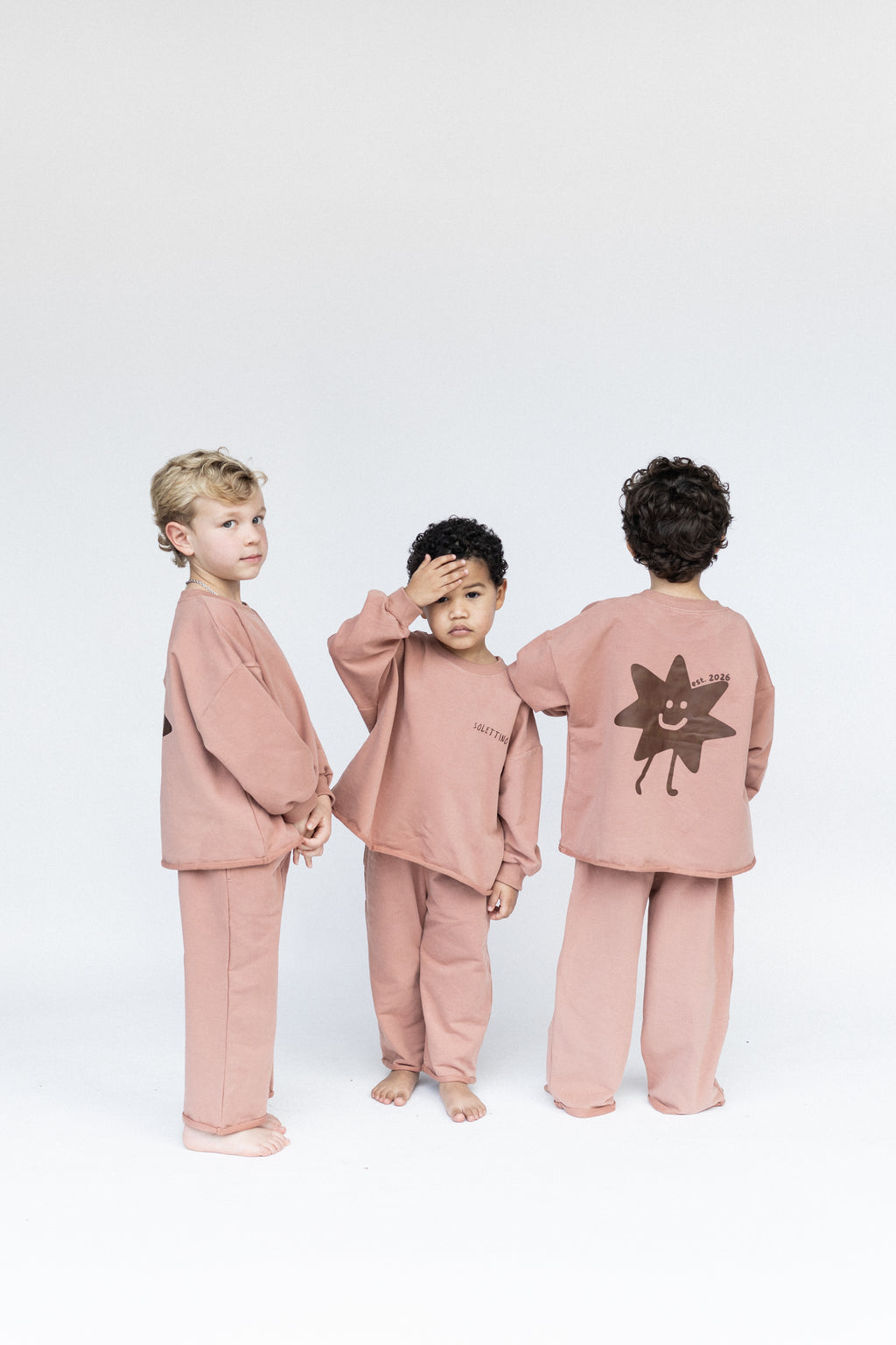 Three children wearing matching pink outfits with a sun design on a white background