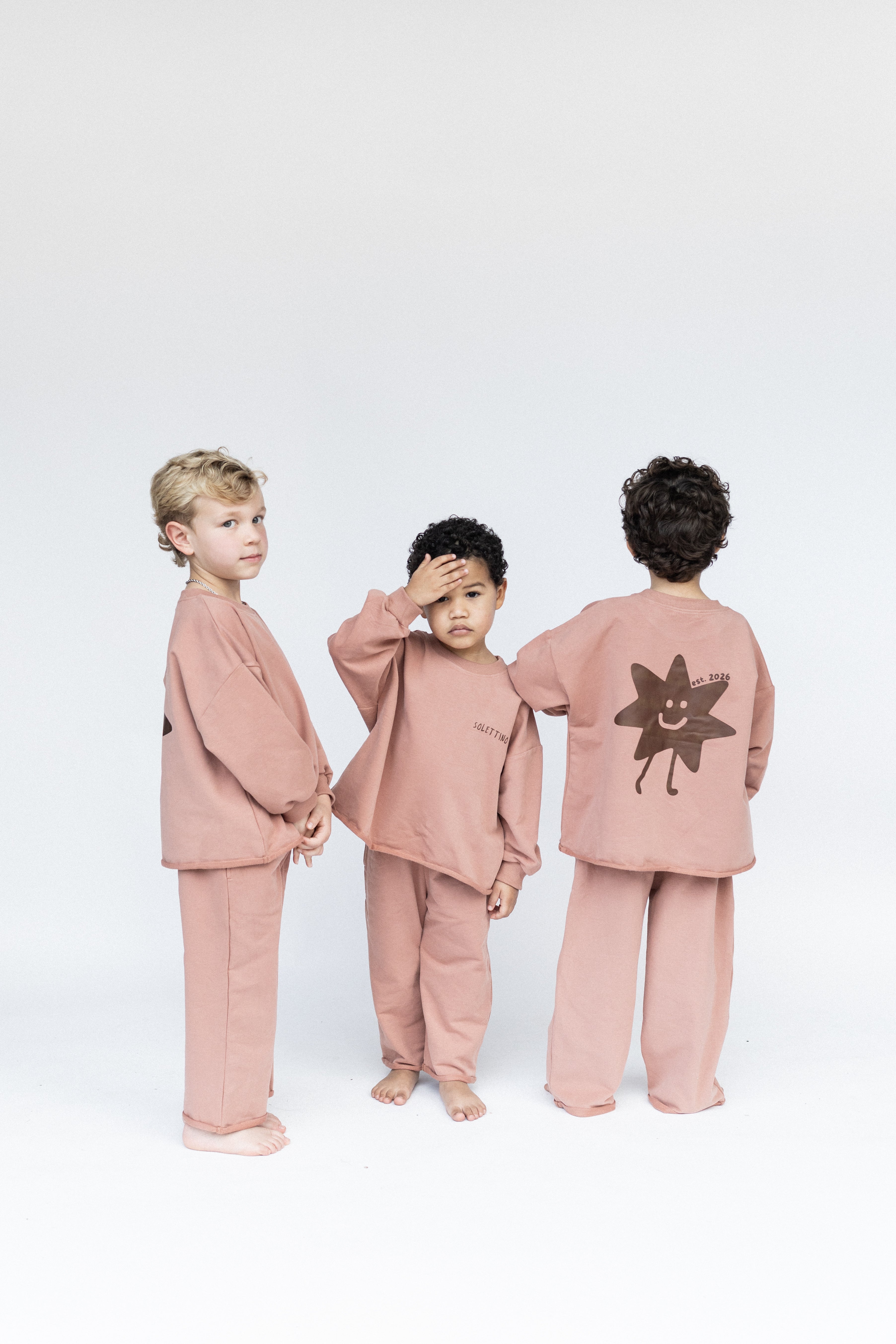 Three children wearing matching pink outfits with a sun design on a white background