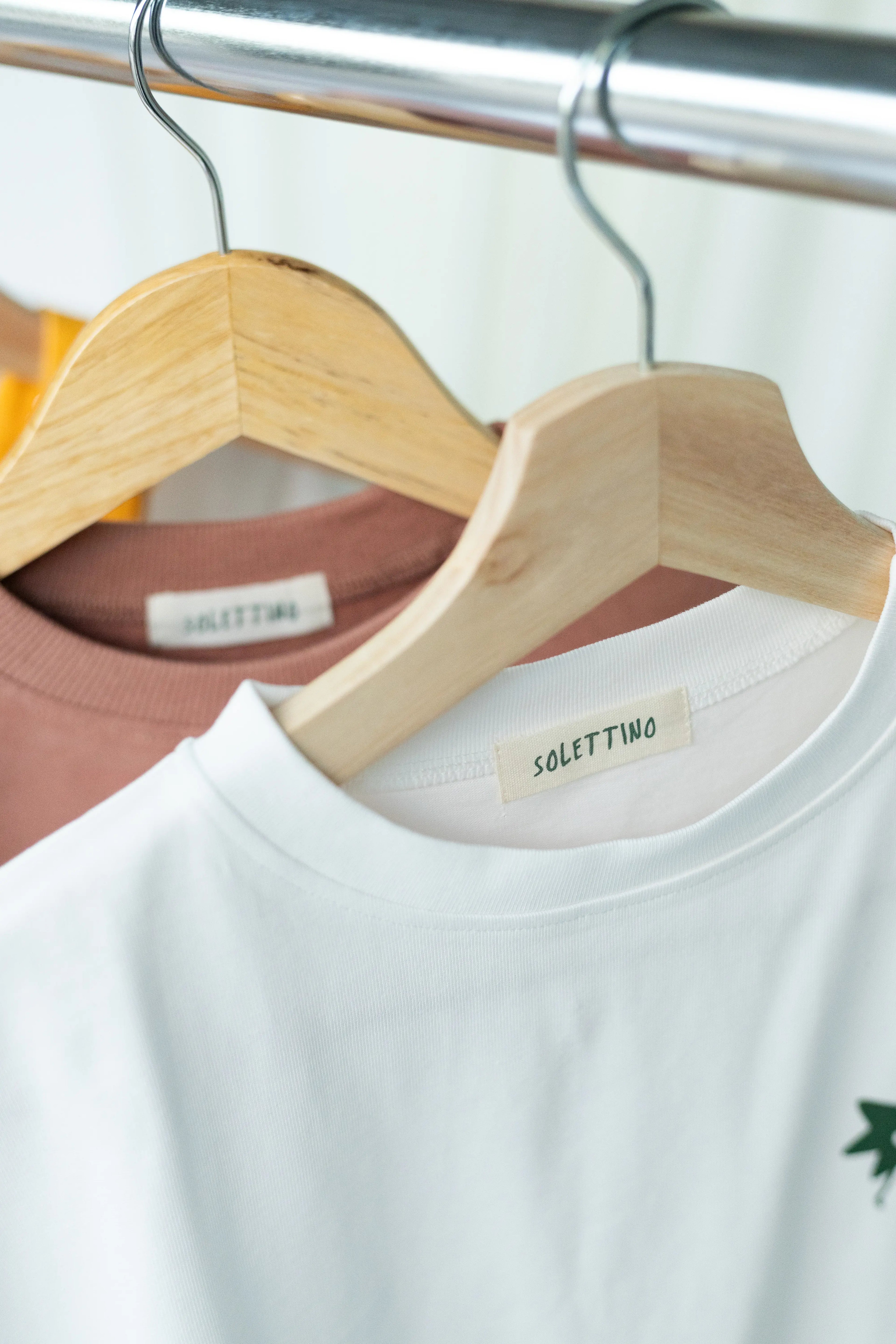 White t-shirt with 'solettwo' label on a wooden hanger against a blurred background