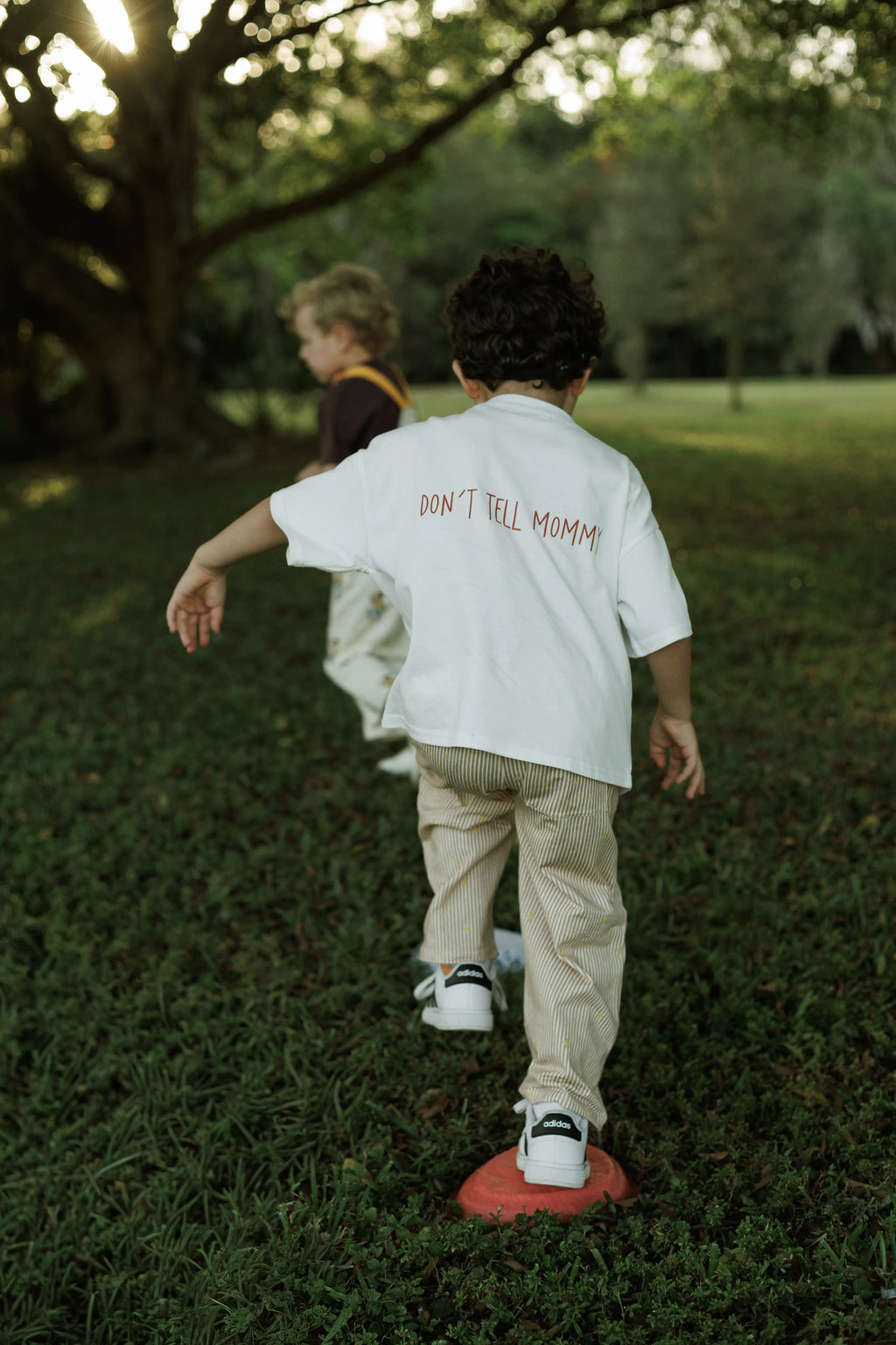 Two children playing outdoors with one wearing a shirt that says 'Don't Tell Mommy'.