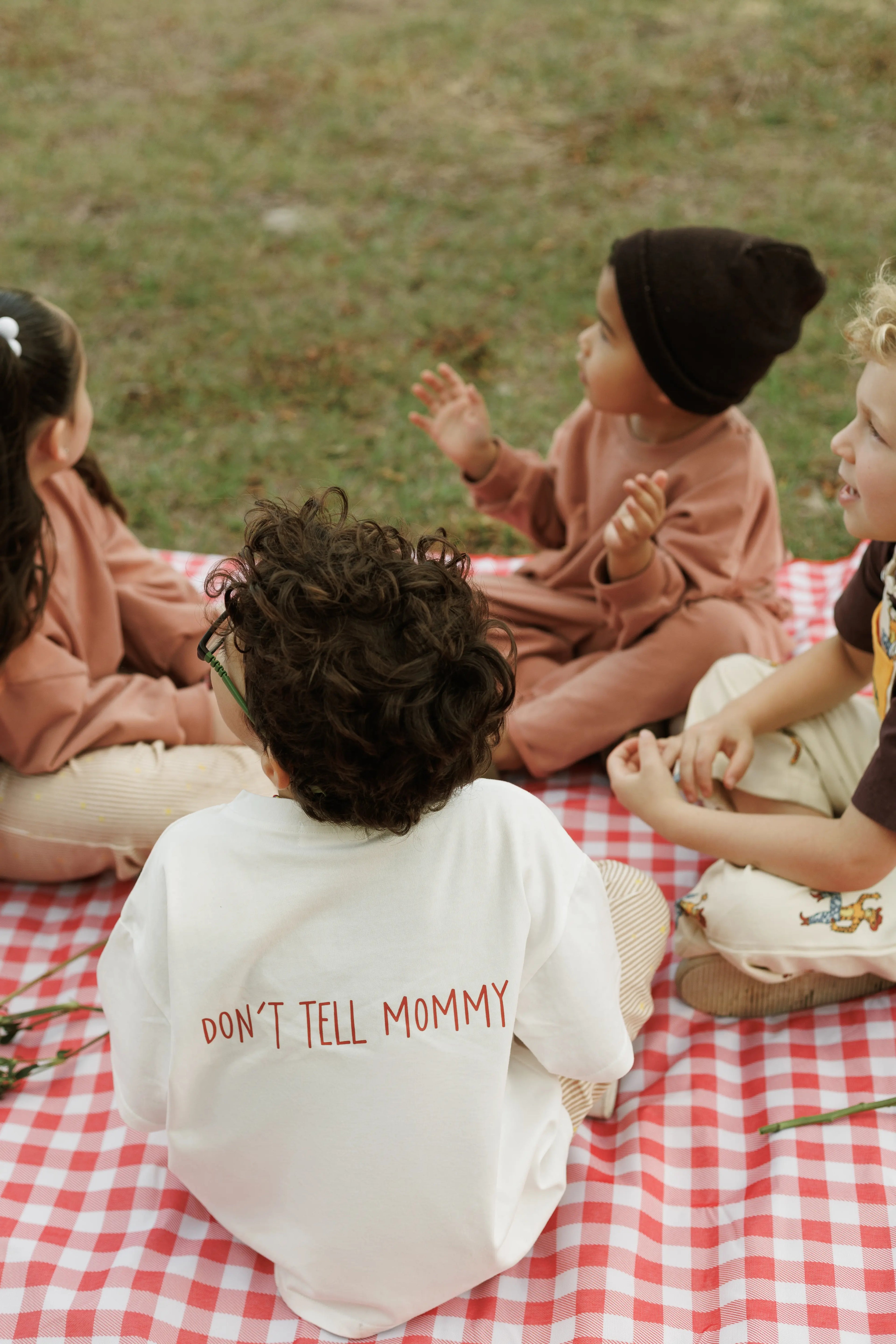 Children sitting on a red and white checkered blanket outdoors.