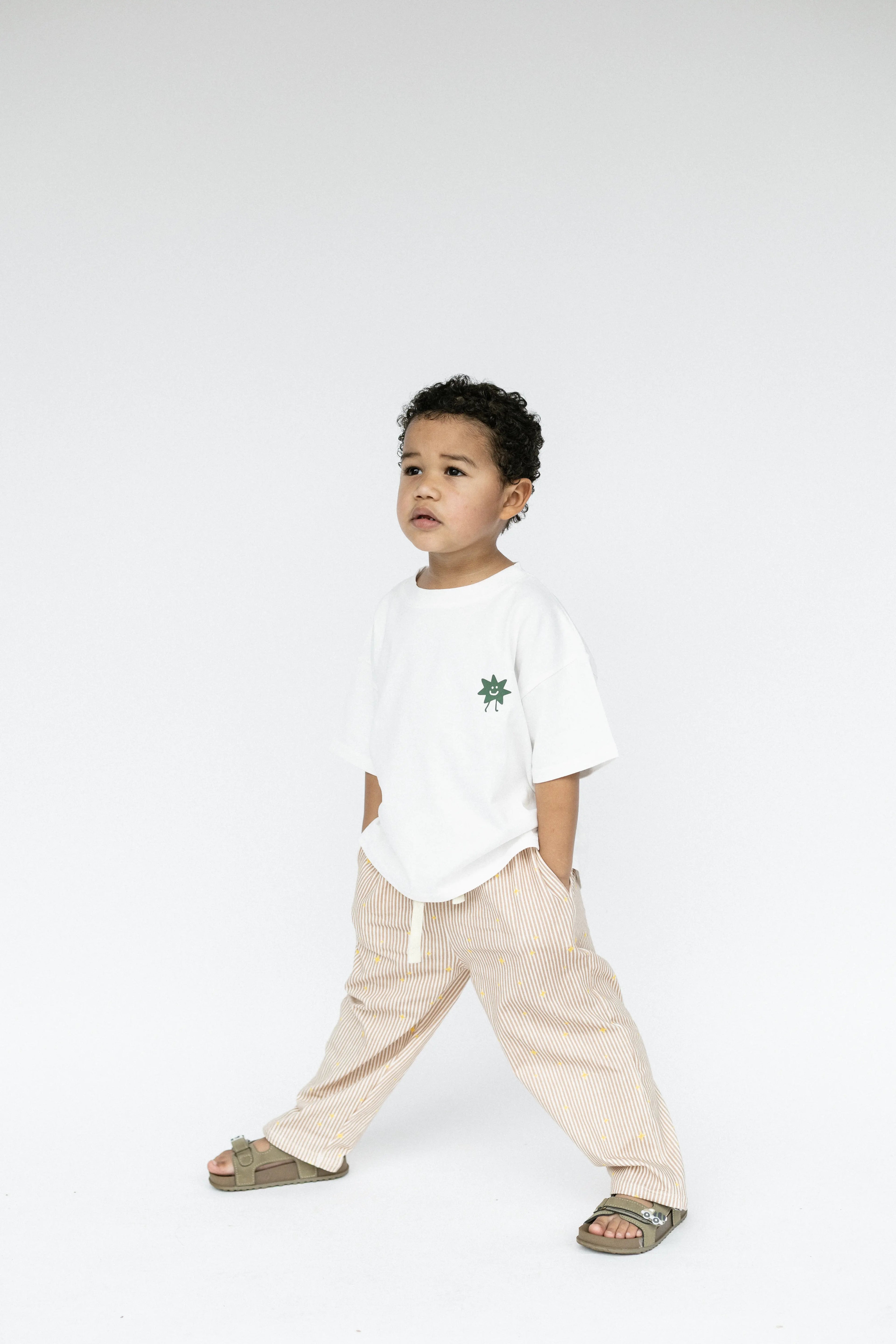 Child wearing a white t-shirt with a small design and beige pants on a white background