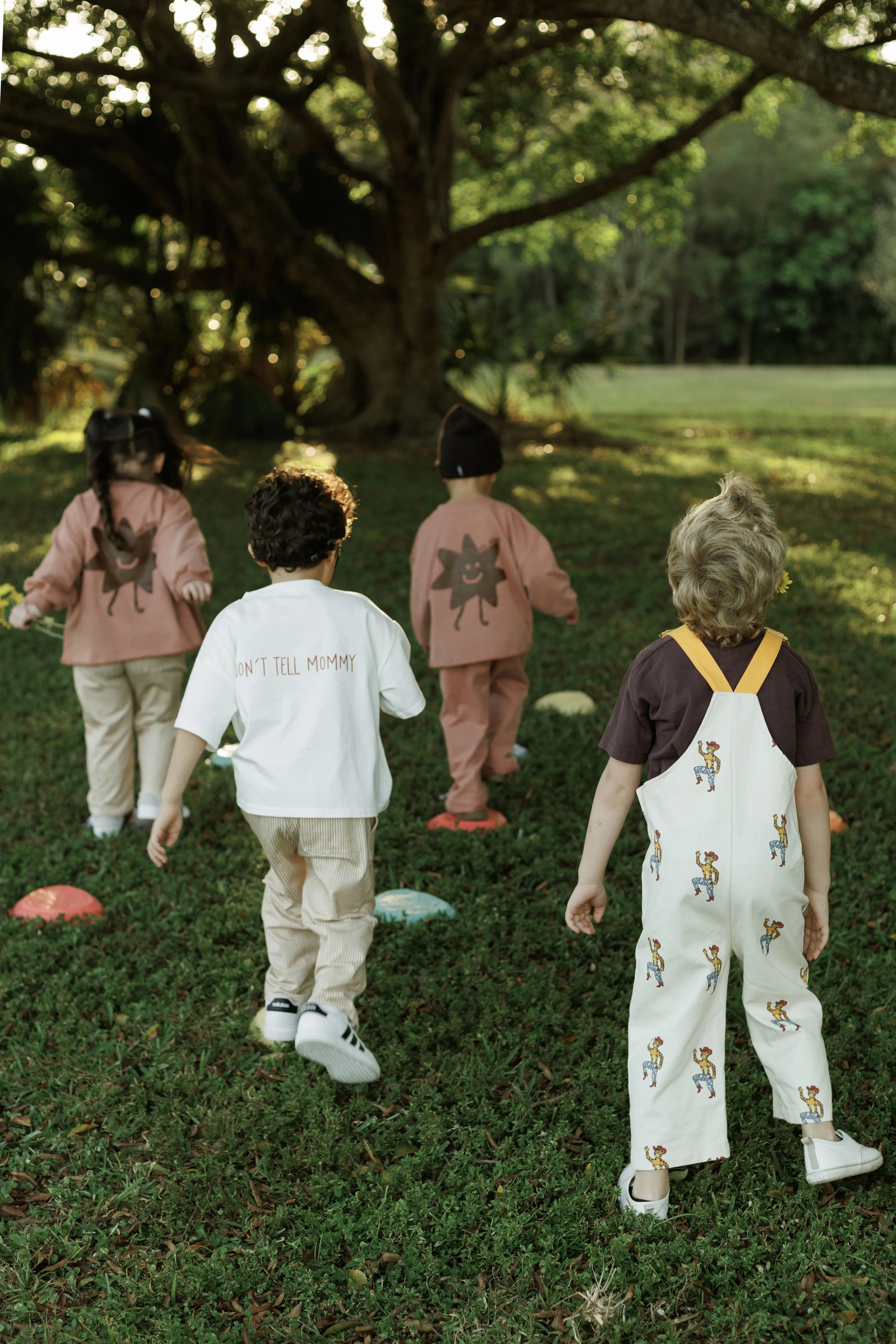 Four children in colorful outfits walking on grass with trees in the background